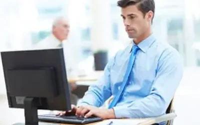 Professional man in blue shirt and tie using computer at desk.