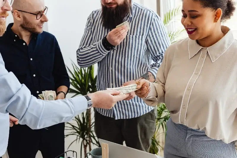 A diverse group of individuals standing around a desk filled with money.