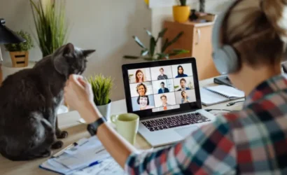 A woman working on a laptop with a cat sitting next to her.