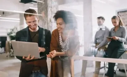 Two people standing in front of a glass wall, working on a laptop together.