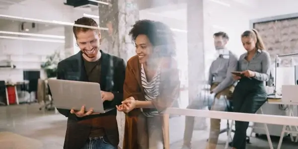 Two people standing in front of a glass wall, working on a laptop together.