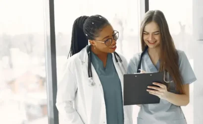 Two women in medical attire analyzing data on a tablet screen.