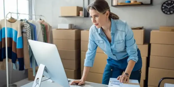 Woman typing on computer surrounded by boxes in room.