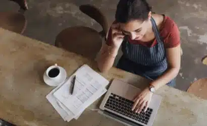 A woman sitting at a table, focused on her laptop screen while working.