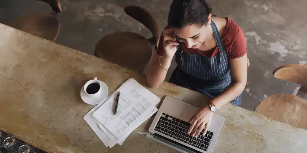 A woman sitting at a table, focused on her laptop screen while working.