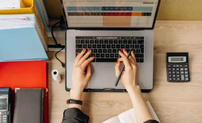 A woman's hands on a laptop, calculator, and office supplies, indicating work or productivity.