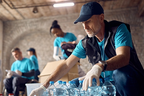 Man in blue shirt and vest packing water bottles in box.